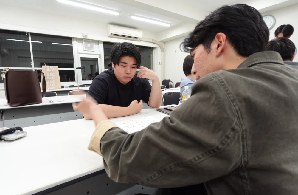 白い長机を挟んで、向かい合って話すACT-Rのメンバー。手前の人が身を乗り出して紙を指さし、奥の人が頬に手を当てて聞いている