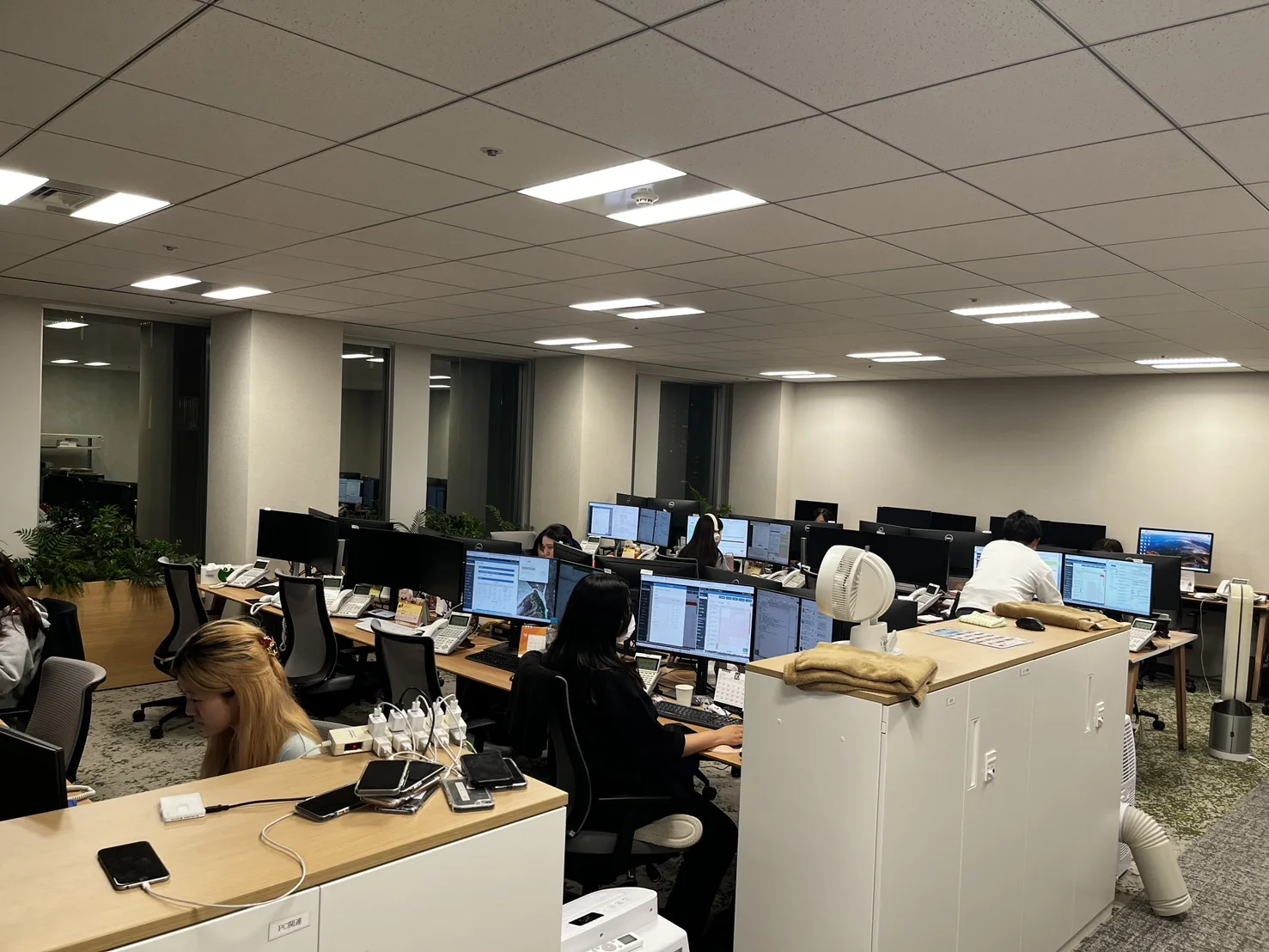 新宿野村ビル26階の執務室。モニターが並ぶ席で、社員が電話を受けたり画面に向かったりしている